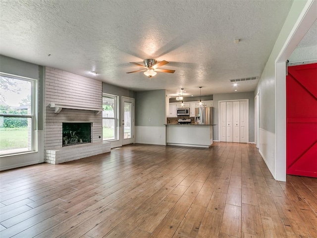 2916 Prairie Rose Ct, Oklahoma City, OK 73120 - unfurnished living room with a ceiling fan, a textured ceiling, a fireplace, a wainscoted wall, and wood finished floors