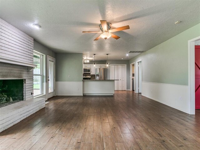 2916 Prairie Rose Ct, Oklahoma City, OK 73120 - unfurnished living room featuring a ceiling fan, a textured ceiling, a fireplace, wainscoting, and dark wood finished floors