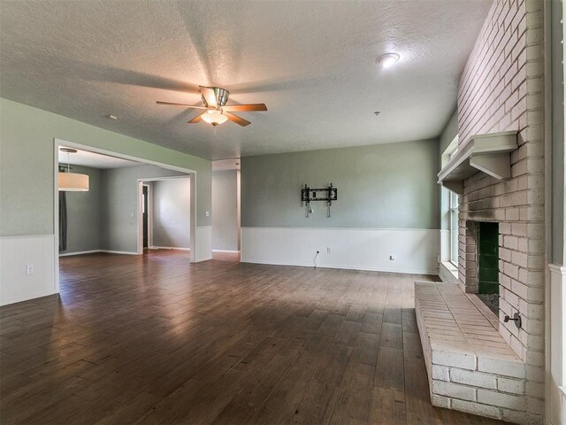 2916 Prairie Rose Ct, Oklahoma City, OK 73120 - unfurnished living room featuring ceiling fan, a textured ceiling, a brick fireplace, a wainscoted wall, and dark wood-style floors