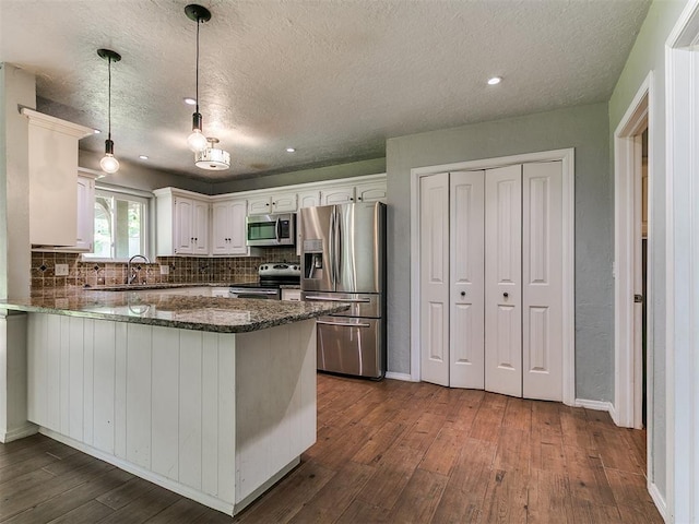 2916 Prairie Rose Ct, Oklahoma City, OK 73120 - kitchen featuring appliances with stainless steel finishes, a peninsula, dark wood-style floors, a sink, and a textured ceiling