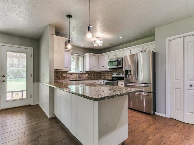 2916 Prairie Rose Ct, Oklahoma City, OK 73120 - kitchen with stainless steel appliances, a peninsula, dark wood-style floors, a textured ceiling, and a sink