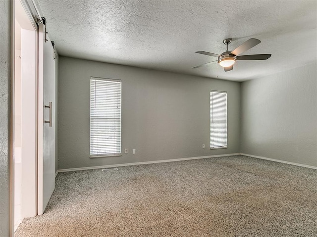 2916 Prairie Rose Ct, Oklahoma City, OK 73120 - carpeted spare room featuring plenty of natural light, ceiling fan, a textured ceiling, baseboards, and a barn door