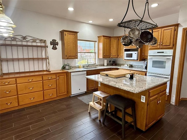 kitchen featuring white appliances, a sink, dark wood-type flooring, a kitchen island, and brown cabinetry