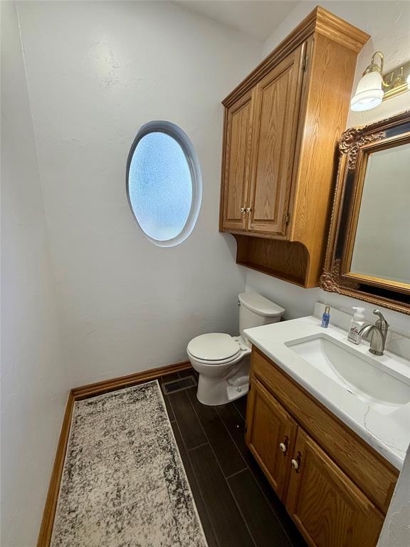 half bath featuring toilet, vanity, wood finished floors, and baseboards