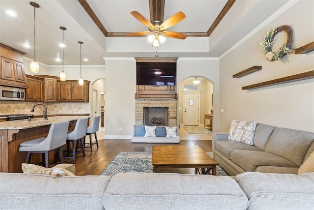19724 Meadow Bend Ave, Edmond, OK 73012 - living room featuring arched walkways, a tray ceiling, dark wood-style flooring, ceiling fan, and ornamental molding