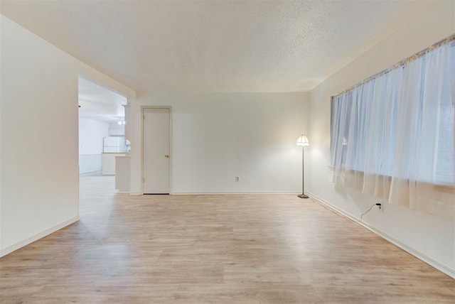 empty room with light wood-style flooring, baseboards, and a textured ceiling