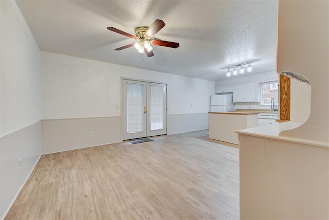 unfurnished living room with a textured ceiling, light wood-style flooring, french doors, a ceiling fan, and rail lighting