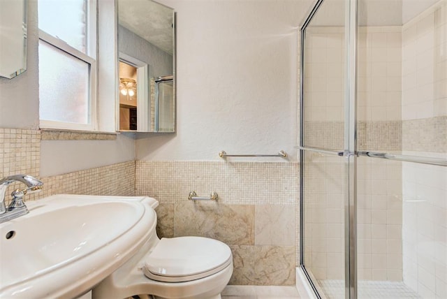 bathroom with a sink, a stall shower, tile walls, toilet, and wainscoting