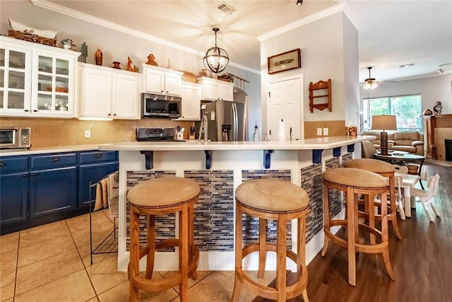 3305 Tecumseh Meadows Way, Norman, OK 73069 - kitchen featuring appliances with stainless steel finishes, blue cabinetry, a breakfast bar, crown molding, and white cabinetry