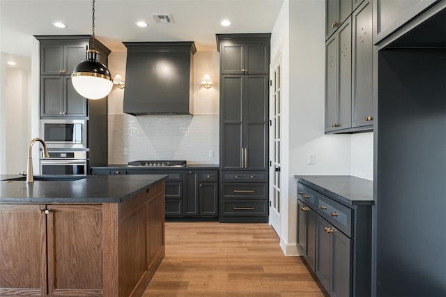 9213 NW 85th St, Yukon, OK 73099 - kitchen featuring dark countertops, appliances with stainless steel finishes, light wood-style floors, custom exhaust hood, and backsplash