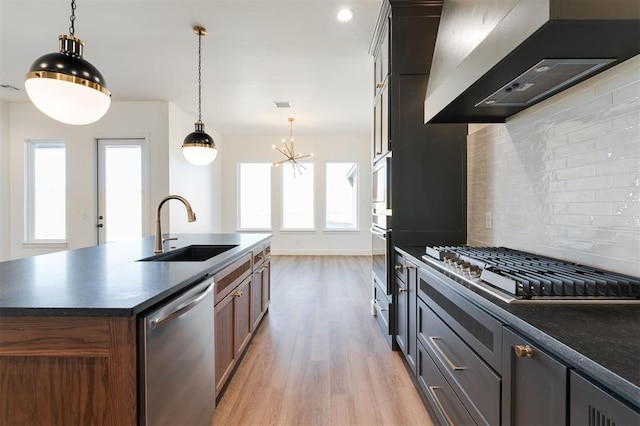 9213 NW 85th St, Yukon, OK 73099 - kitchen with a sink, appliances with stainless steel finishes, wall chimney range hood, dark countertops, and light wood-type flooring