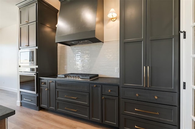 9213 NW 85th St, Yukon, OK 73099 - kitchen featuring range hood, appliances with stainless steel finishes, dark countertops, tasteful backsplash, and light wood finished floors