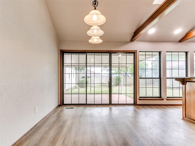 unfurnished dining area with wood finished floors, beam ceiling, and baseboards
