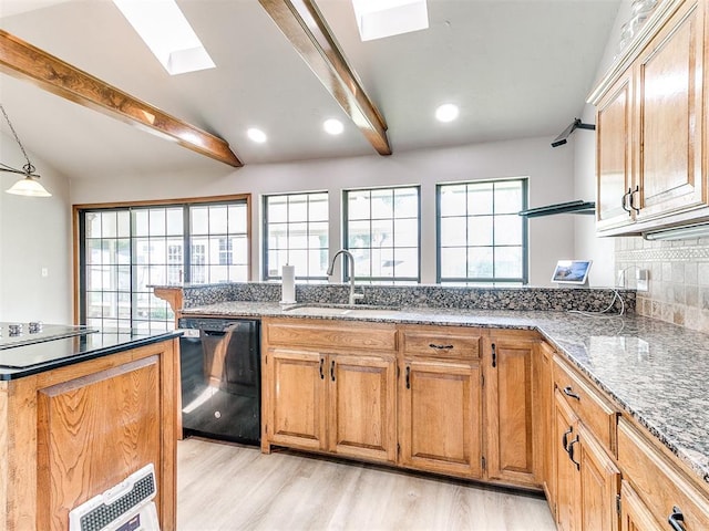 kitchen featuring black dishwasher, a sink, a skylight, light wood-style floors, and dark stone countertops