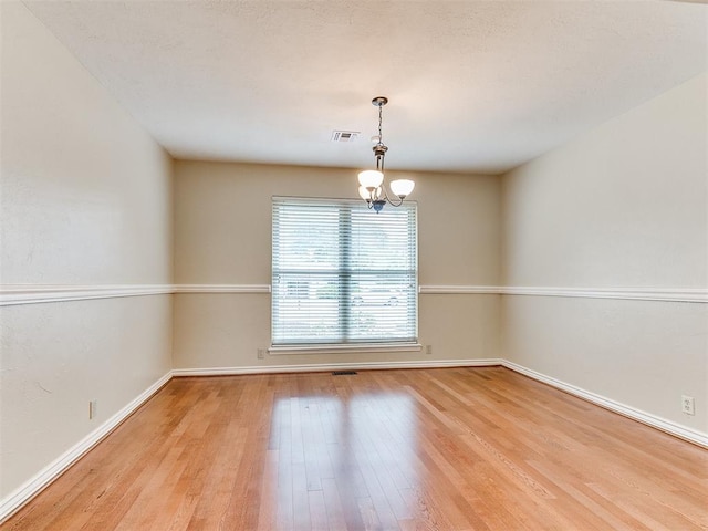 unfurnished room featuring wood finished floors, a chandelier, and baseboards
