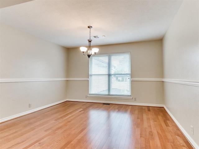 empty room featuring wood finished floors, a chandelier, and baseboards