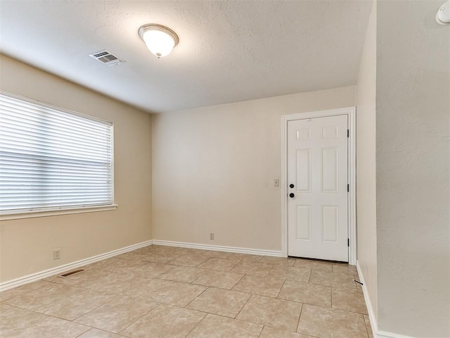 spare room with a textured ceiling, baseboards, and light tile patterned flooring