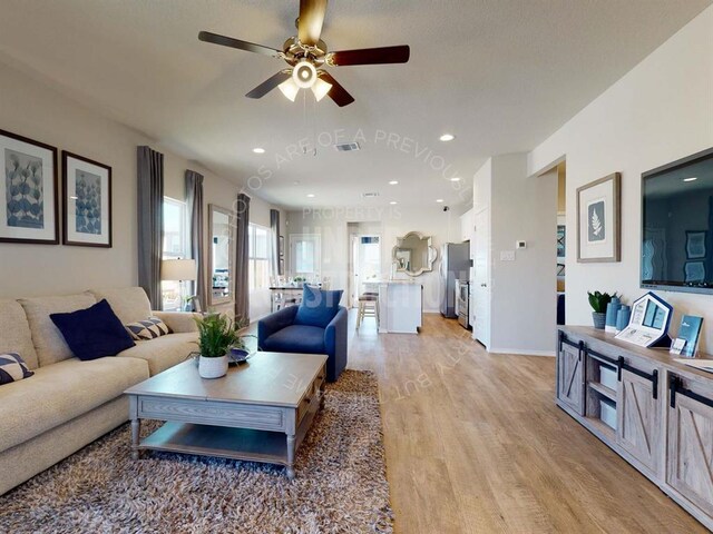 living area with light wood-style flooring, healthy amount of natural light, a ceiling fan, recessed lighting, and baseboards