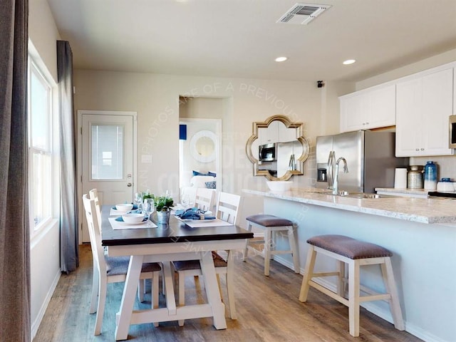 kitchen featuring white cabinets, light stone countertops, stainless steel appliances, a kitchen breakfast bar, and light wood-style flooring