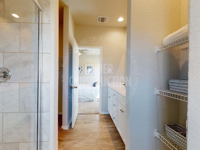 ensuite bathroom with wood finished floors, a shower stall, vanity, and recessed lighting
