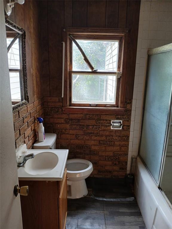 bathroom with toilet, healthy amount of natural light, vanity, and bath / shower combo with glass door