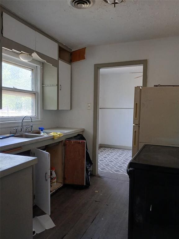 kitchen featuring freestanding refrigerator, white cabinetry, dark wood-style flooring, a sink, and light countertops