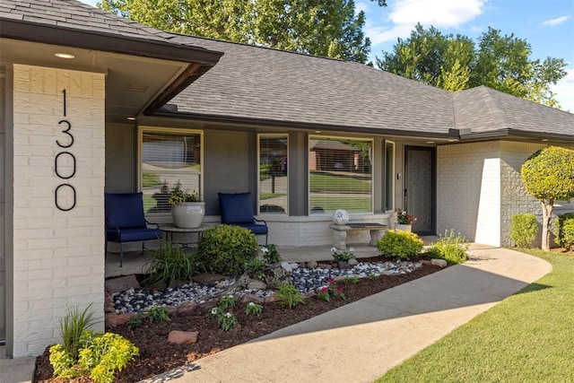 view of front of home featuring a shingled roof, brick siding, and a porch