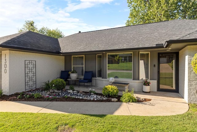 entrance to property with brick siding, roof with shingles, and covered porch