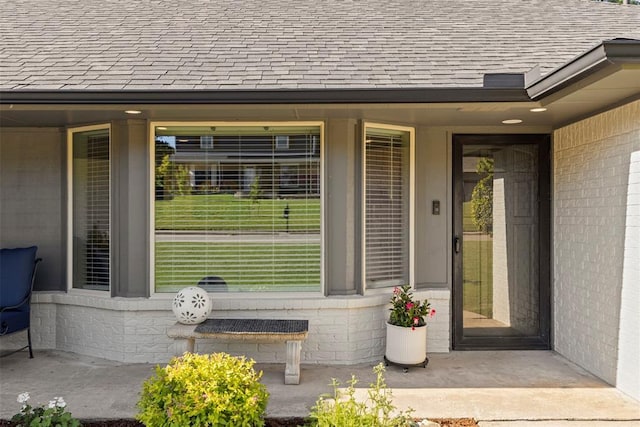 doorway to property featuring roof with shingles and brick siding