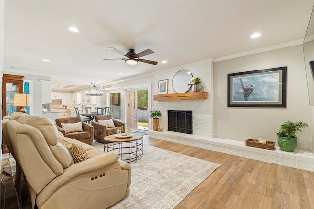 living area with crown molding, a ceiling fan, recessed lighting, light wood-type flooring, and a brick fireplace