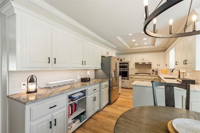 kitchen with a sink, stainless steel appliances, light wood finished floors, white cabinetry, and crown molding