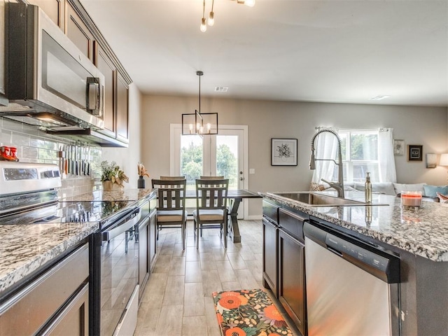 kitchen featuring stainless steel appliances, a sink, a chandelier, open floor plan, and hanging light fixtures