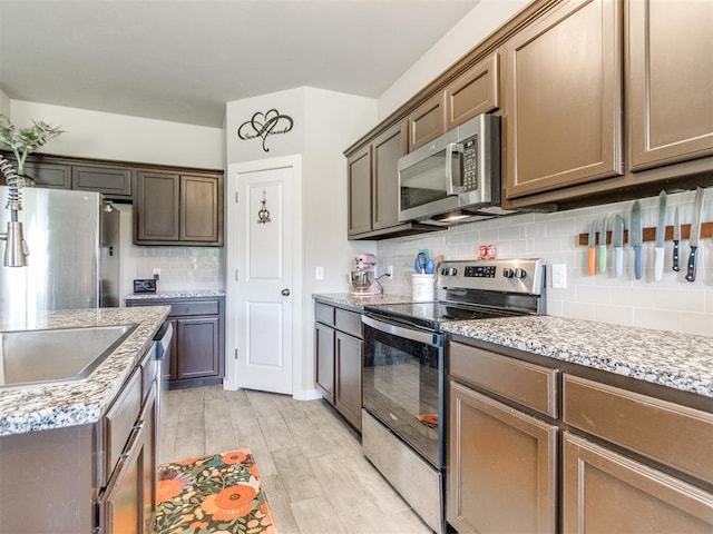 kitchen with stainless steel appliances, tasteful backsplash, light wood finished floors, and light stone counters