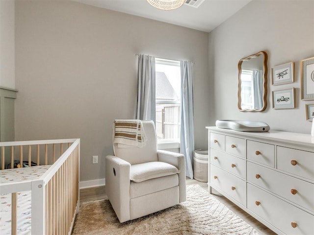 bedroom with a nursery area, light wood-style flooring, and baseboards