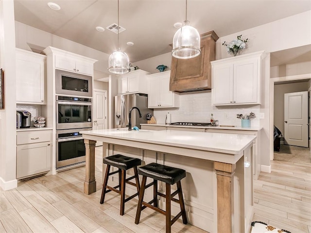 kitchen featuring a sink, appliances with stainless steel finishes, light countertops, tasteful backsplash, and light wood finished floors