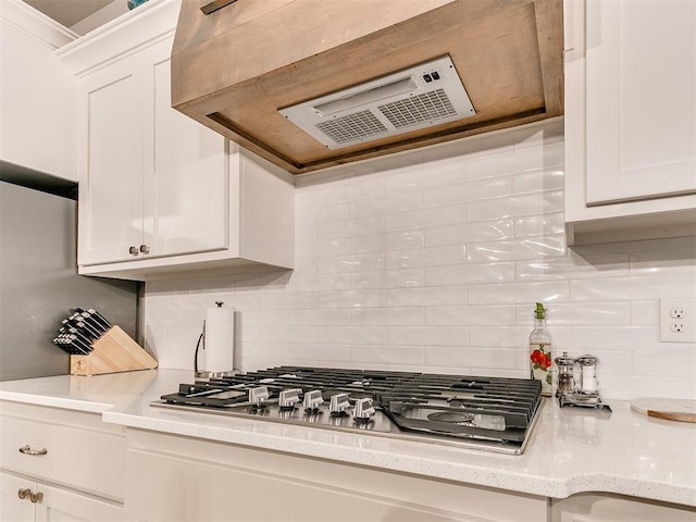 kitchen with stainless steel gas cooktop, exhaust hood, white cabinets, and backsplash