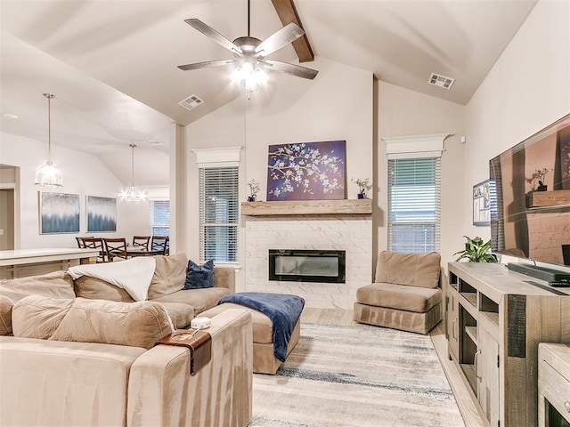 living area featuring a stone fireplace, ceiling fan, healthy amount of natural light, beam ceiling, and high vaulted ceiling
