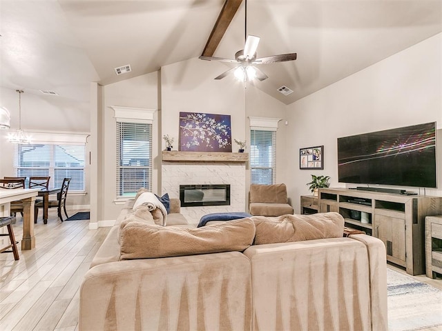 living area with a stone fireplace, a ceiling fan, healthy amount of natural light, light wood-style flooring, and beamed ceiling