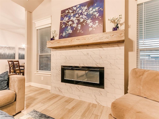 living area featuring a tile fireplace, wood finished floors, baseboards, and vaulted ceiling