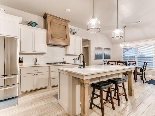 kitchen featuring appliances with stainless steel finishes, decorative backsplash, light countertops, a kitchen bar, and light wood-style flooring