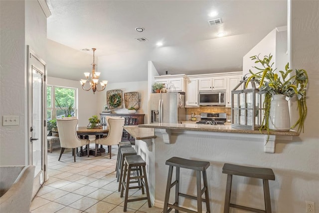 13141 Austrian Pine Dr, Choctaw, OK 73020 - kitchen featuring stainless steel appliances, a peninsula, light tile patterned floors, a kitchen bar, and backsplash