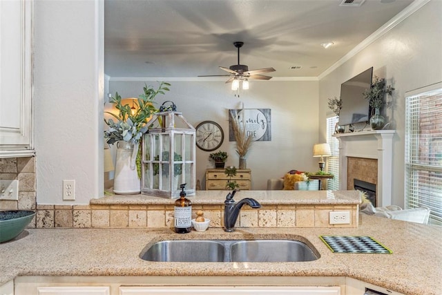 13141 Austrian Pine Dr, Choctaw, OK 73020 - kitchen featuring a sink, a fireplace, ceiling fan, ornamental molding, and white cabinets