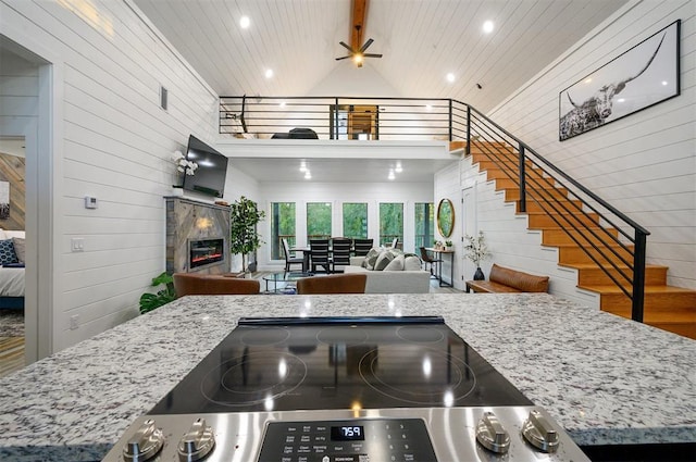 48 Cedar Hills Trl, Broken Bow, OK 74728 - kitchen featuring wooden walls, open floor plan, a glass covered fireplace, light stone counters, and high vaulted ceiling