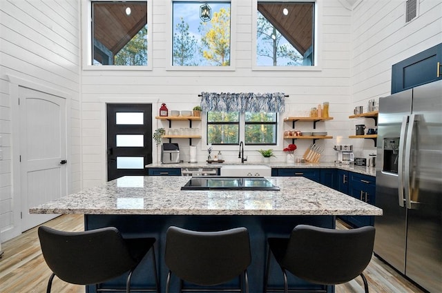 48 Cedar Hills Trl, Broken Bow, OK 74728 - kitchen with stainless steel fridge with ice dispenser, blue cabinetry, open shelves, high vaulted ceiling, and a sink