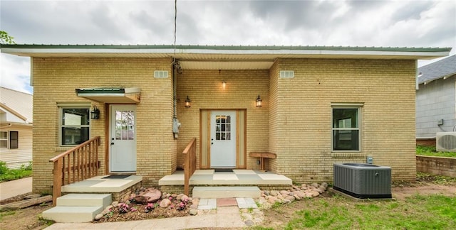 rear view of property with central air condition unit, brick siding, and metal roof