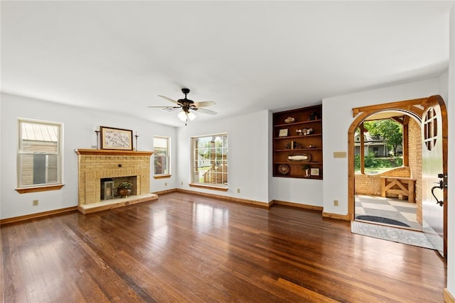 unfurnished living room with plenty of natural light, wood finished floors, a ceiling fan, and a fireplace