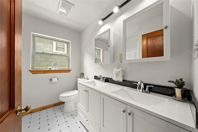 bathroom featuring toilet, tile patterned floors, double vanity, and baseboards