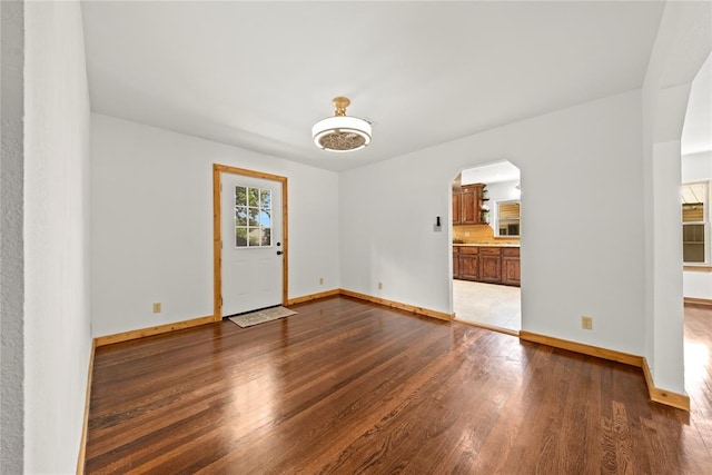 empty room with wood finished floors, arched walkways, and baseboards