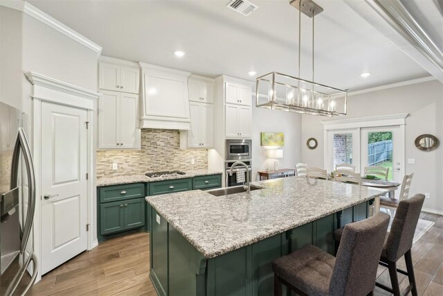 8400 Poplar Dr, Edmond, OK 73034 - kitchen with green cabinetry, appliances with stainless steel finishes, wood finished floors, a kitchen breakfast bar, and crown molding