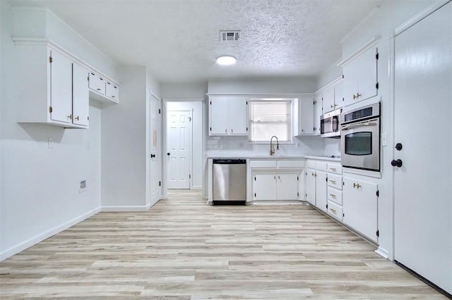 2528 Oakridge Dr, Bethany, OK 73008 - kitchen with appliances with stainless steel finishes, white cabinetry, light countertops, light wood-type flooring, and a textured ceiling